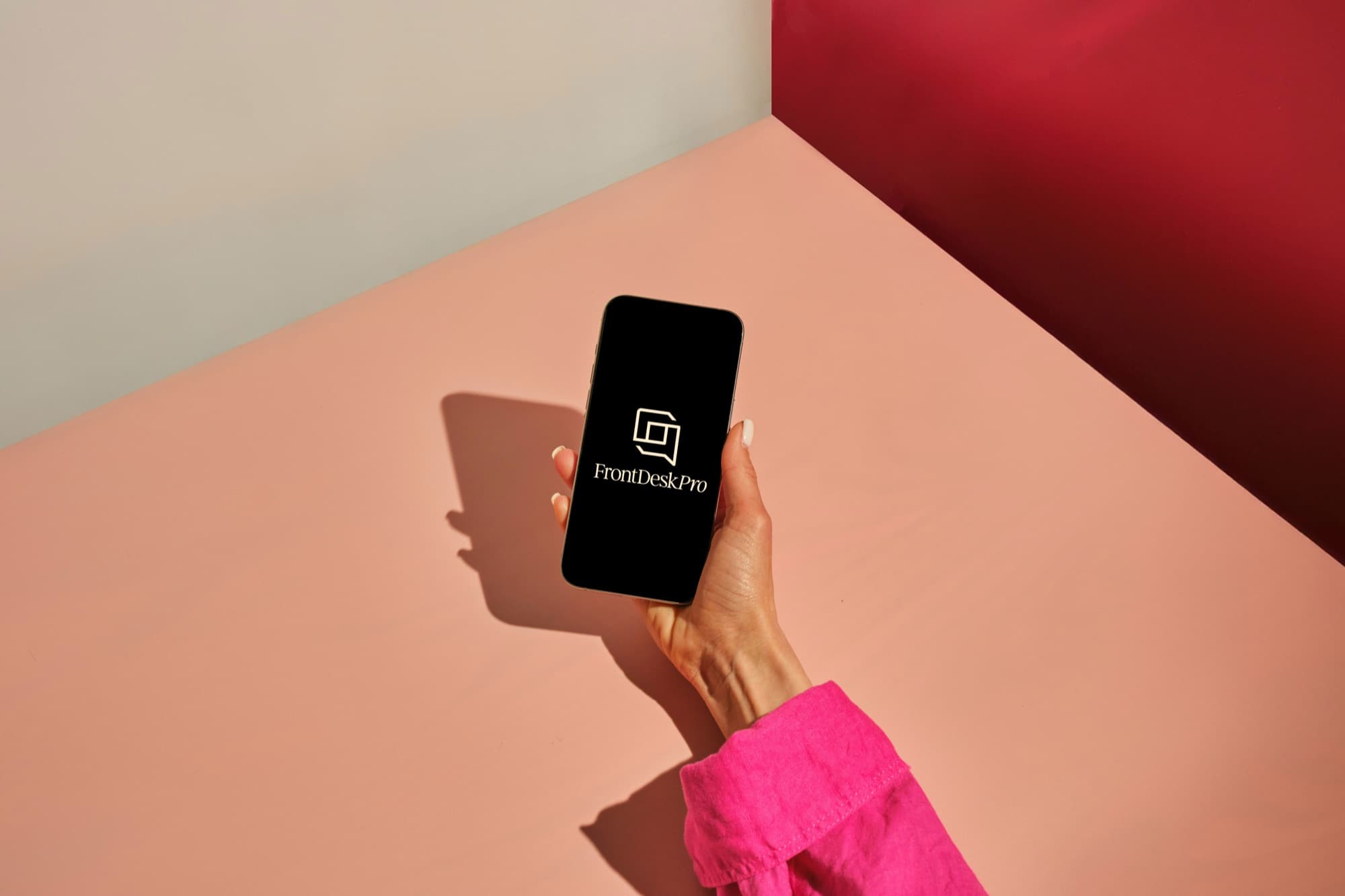 A hand holding a phone showing the FrontDeskPro logo